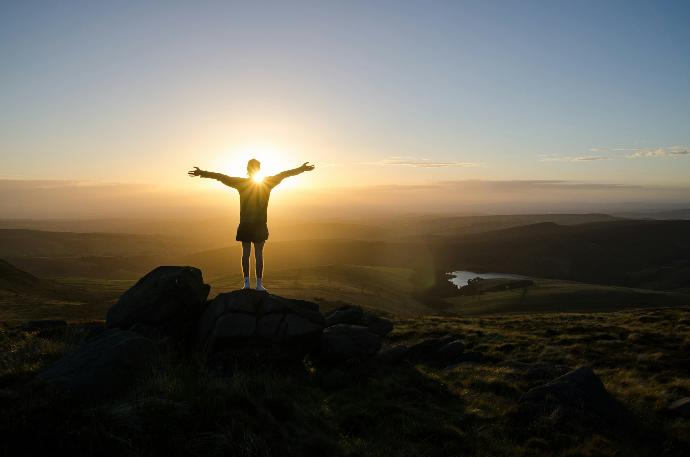 silhouette of person standing on rock during sunset